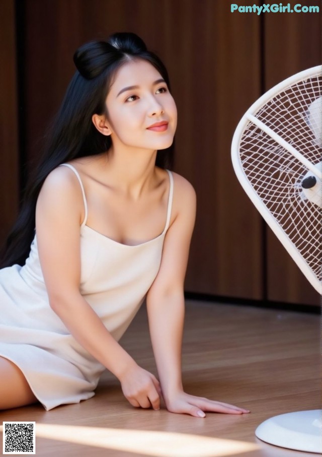 A woman in a white dress sitting on the floor next to a fan.