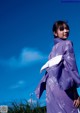 A woman in a purple kimono standing in a field.