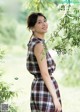 A woman in a plaid dress standing under a tree.