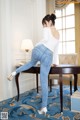 A woman in a white top and blue jeans is bending over a table.