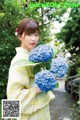 A woman in a yellow kimono holding a bunch of blue flowers.